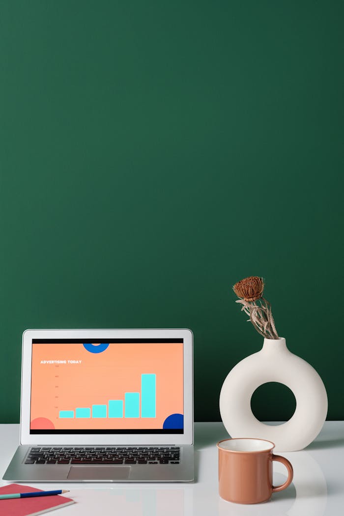 who-we-are A minimalist workspace featuring a laptop with graphs, a stylish vase, and a coffee cup on a sleek surface.